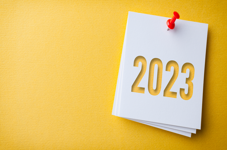 White Sticky Note With Happy New Year 2023 And Red Push Pin On Yellow Cardboard Background