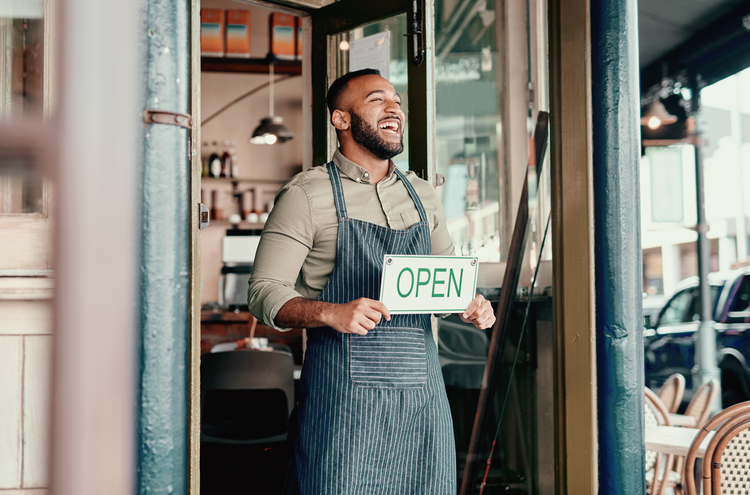 man holding an "open" sign at the doorway of his cafe